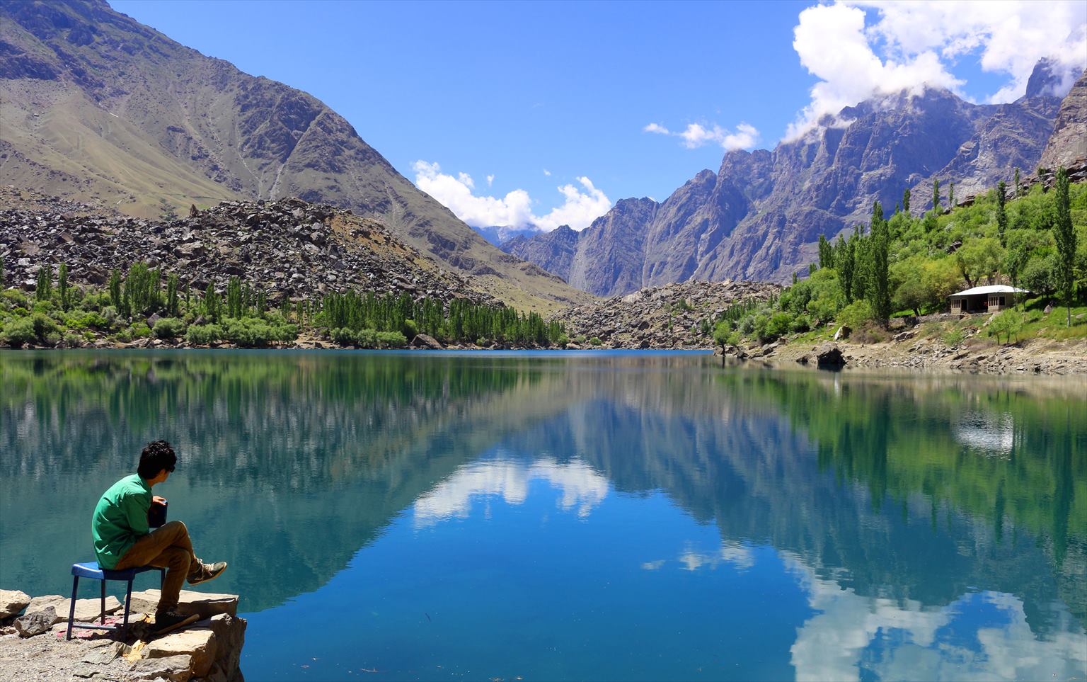 A visitor beside clear Upper Kachura Lake with trees and rocky mountains reflected in the water